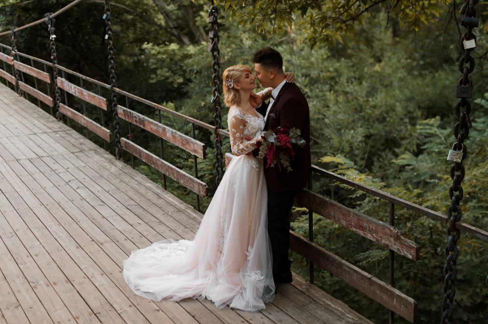 Newlywed couple sharing a romantic moment on a wooden bridge surrounded by nature.